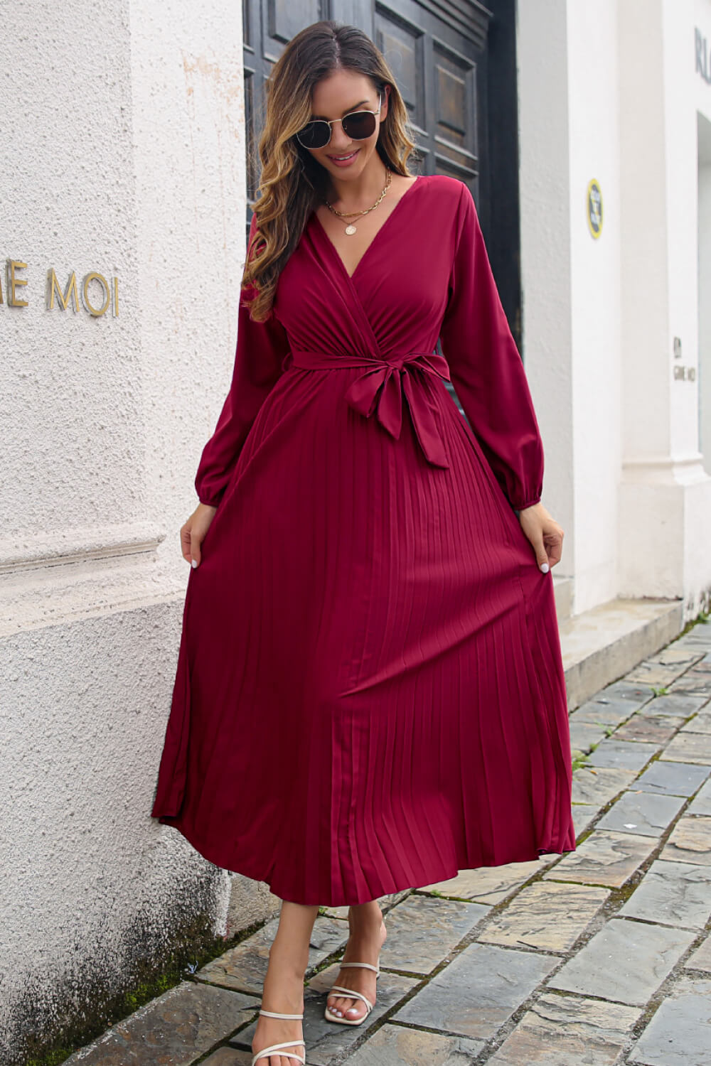 Pleated Long Sleeve Surplice Maxi Dress in burgundy with pleated detailing and waist tie, model wearing stylish sunglasses.