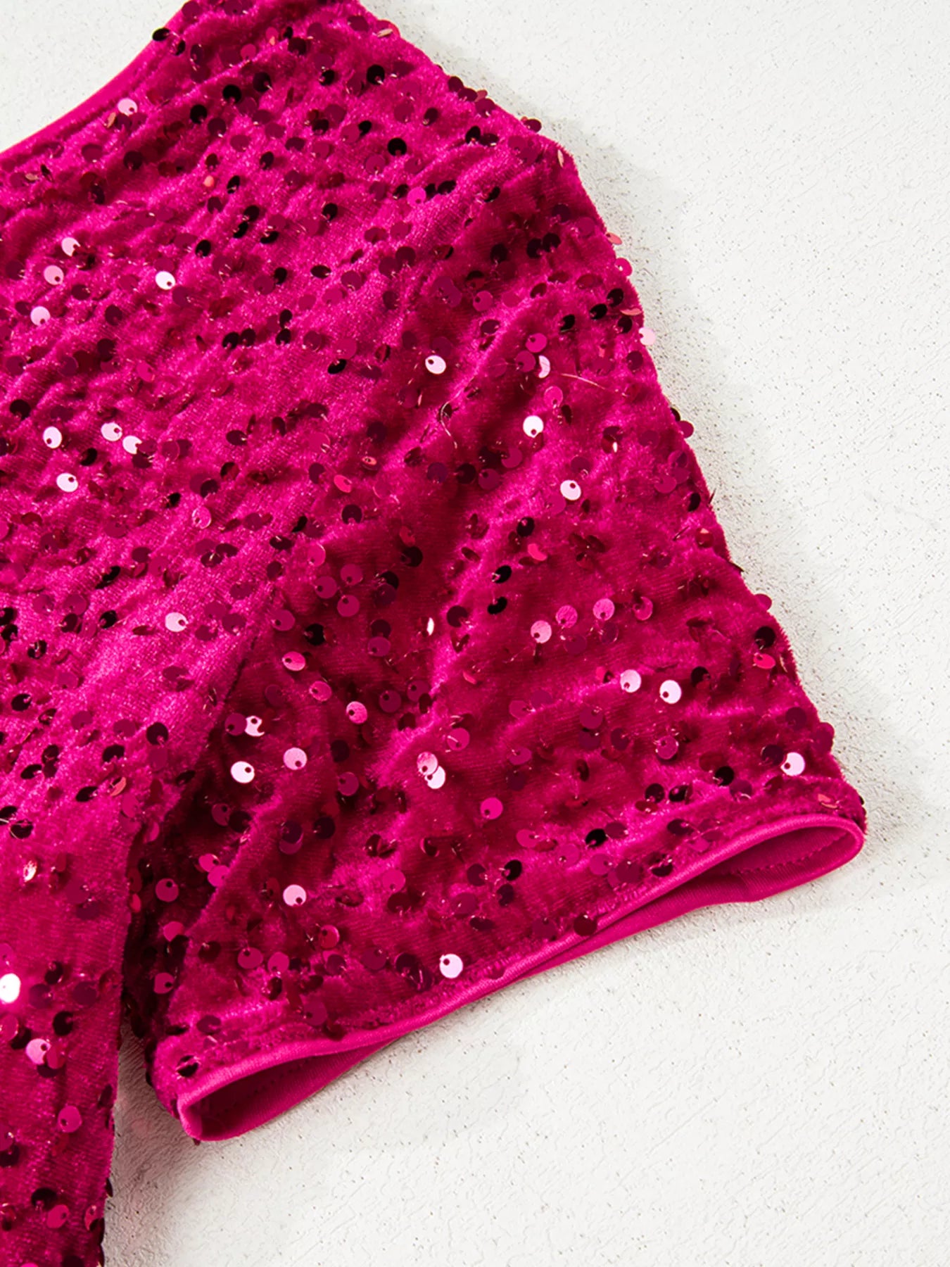 Close-up of vibrant sequin one-shoulder dress fabric, showcasing shiny pink sequins on a textured background.
