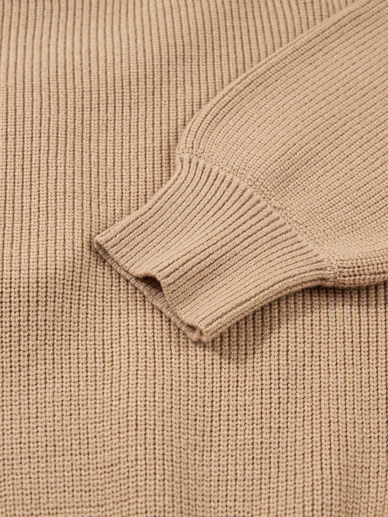 Close-up of a ribbed sleeve from a stylish knit sweater dress for women in beige color.